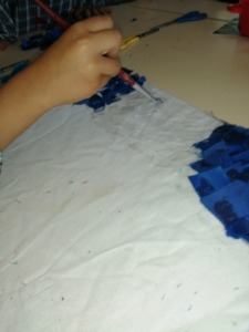 Criança a colar quadradinhos de tecido azul dando forma ao céu