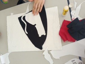 Alunos com o molde do puma em papel. Com a ajuda do molde recortaram o tecido que necessitavam e colavam a cola de batom.