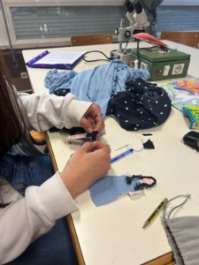 Uma das alunas a coser uma perna da personagem Dorothy Gale feita de cartulina reutilizada e tecido.
