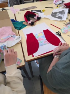 Aluna a costurar a saia da Capuchinho ao lado da base A3 com as primeiras peças da capa do livro.